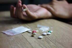 Image of a person's outstretched hand near a collection of pills and other drugs